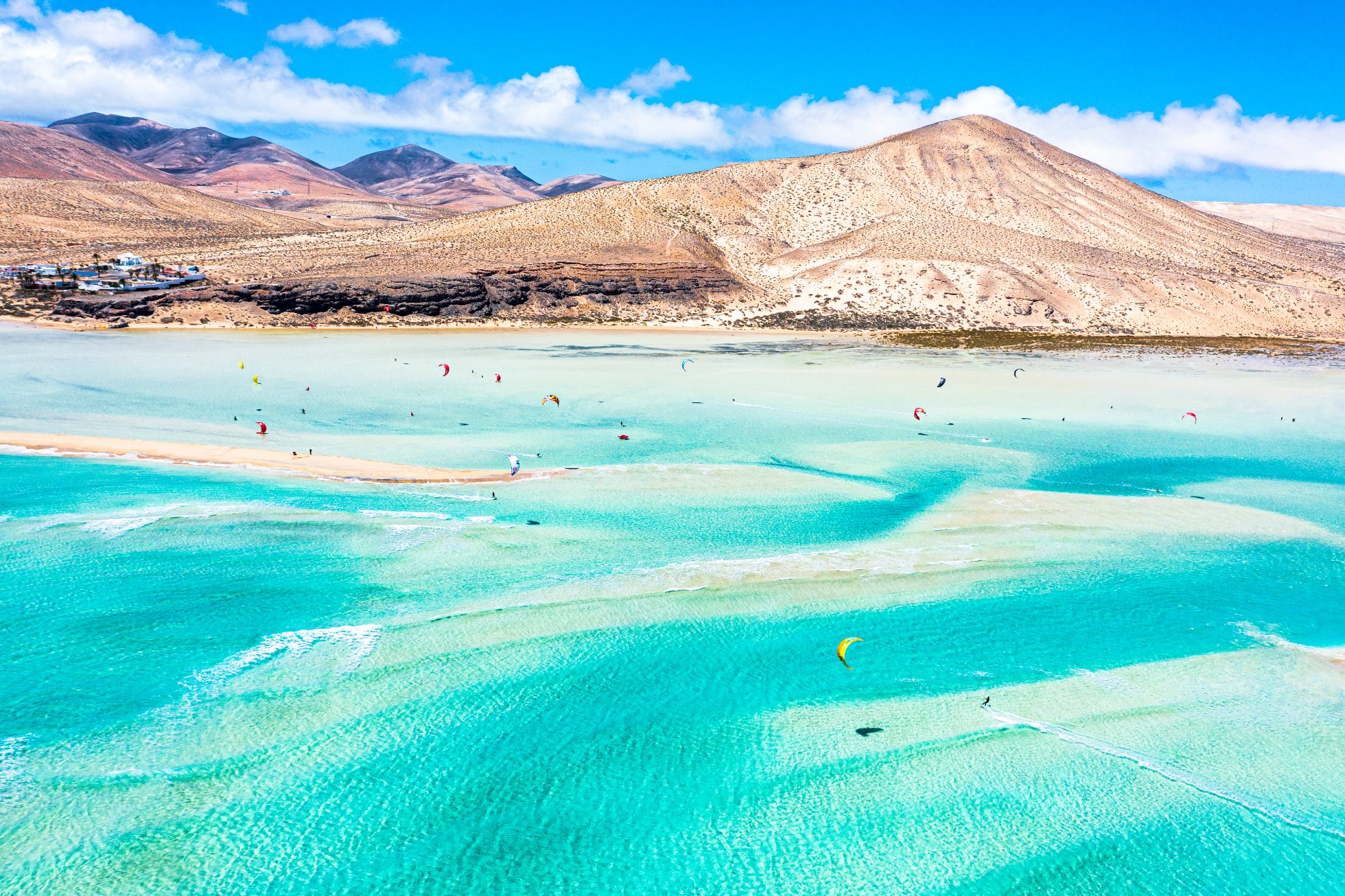 People kiteboarding on waves crashing on white sand of Sotavento beach, Jandia, Fuerteventura, Canary Islands, Spain