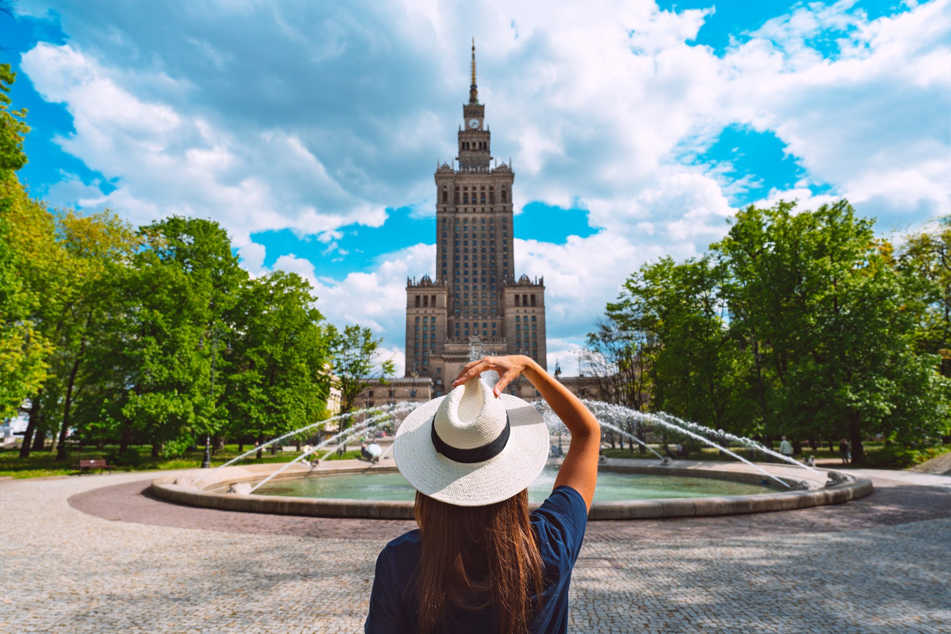 A woman in a white hat by the fountain in front of the Palace of Culture and Science in Warsaw.