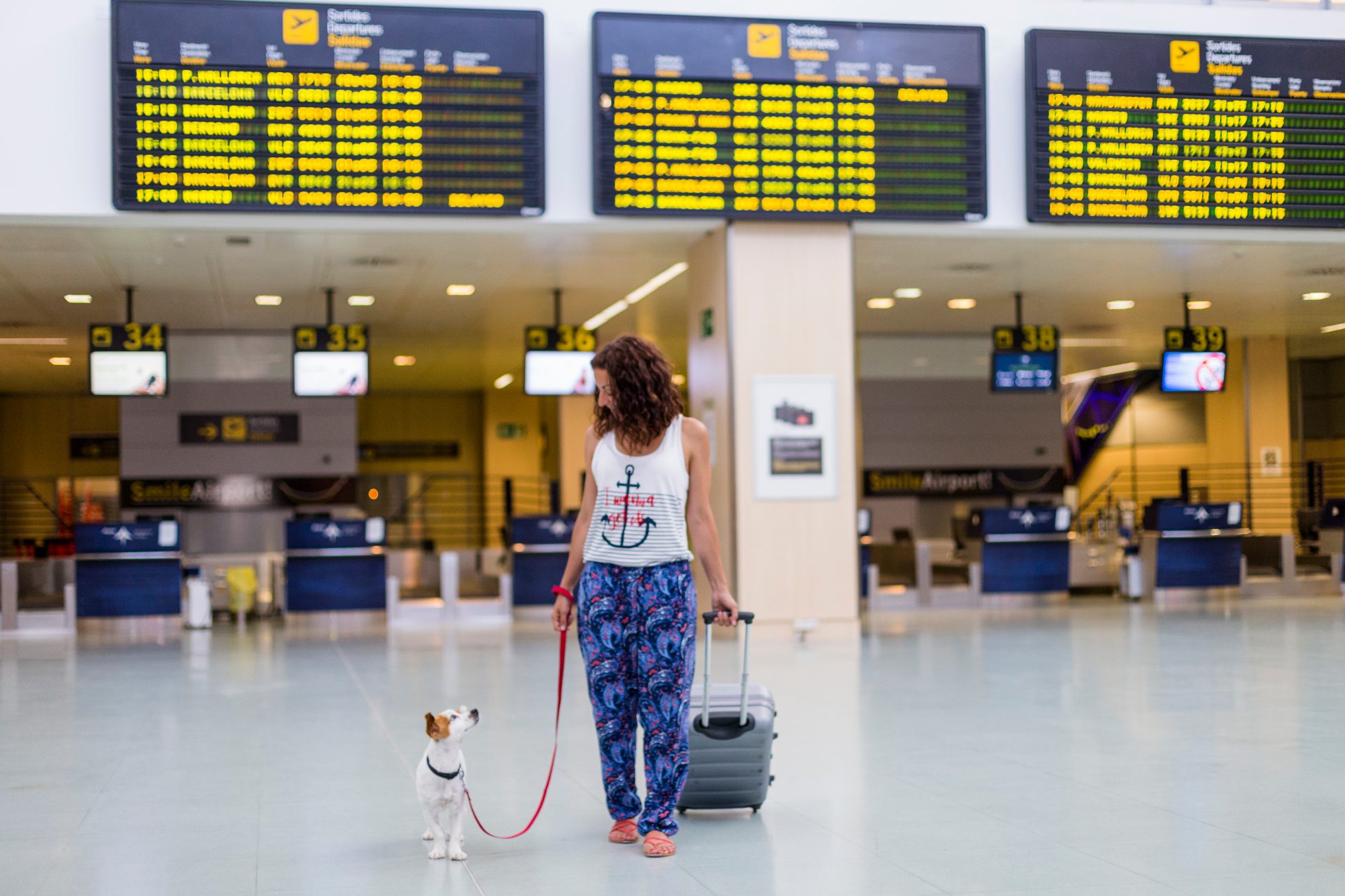 A woman traveling with her dog walking in the airport.