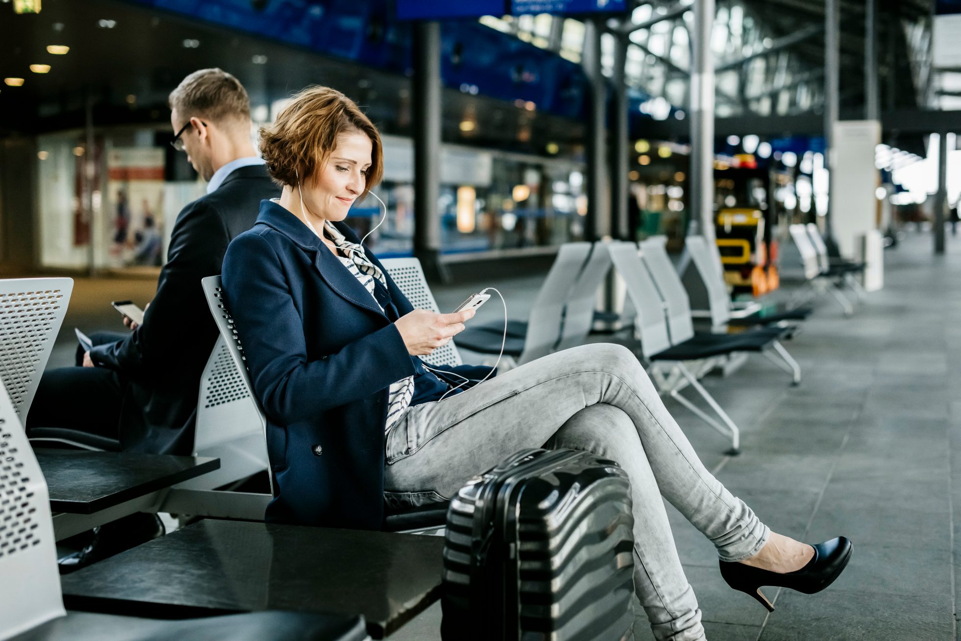 Businesswoman is waiting for the plane, listens to music and browses the phone
