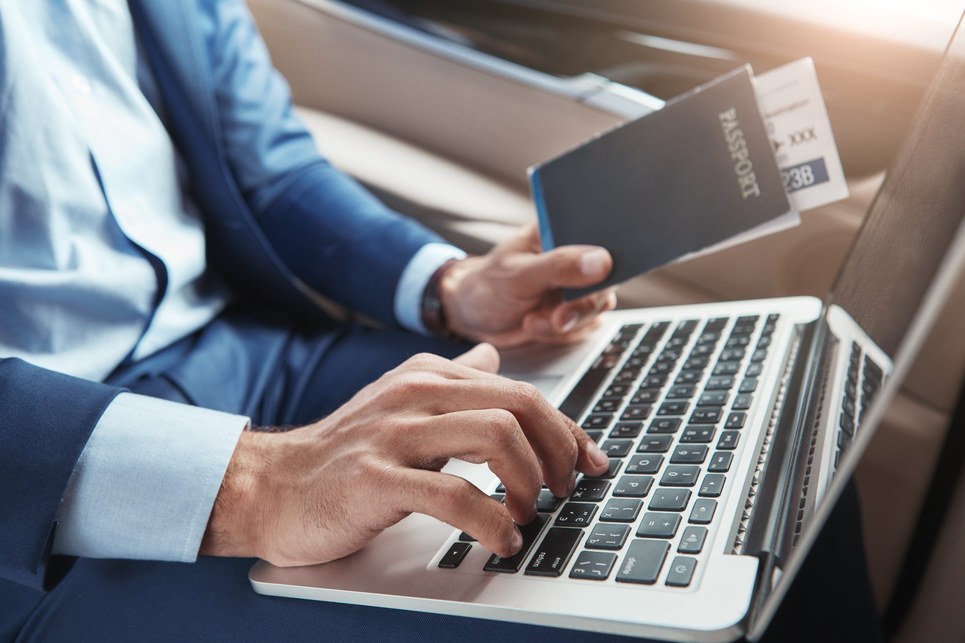 Młody biznesmen w formalnym stroju odprawiający się na laptopie i trzymający paszport z biletami lotniczymi