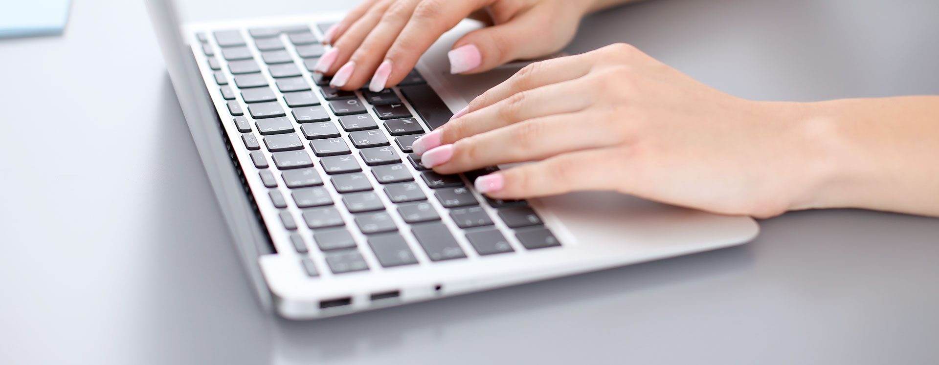 Female hands writing on the keyboard of a silver laptop with black keyboard buttons