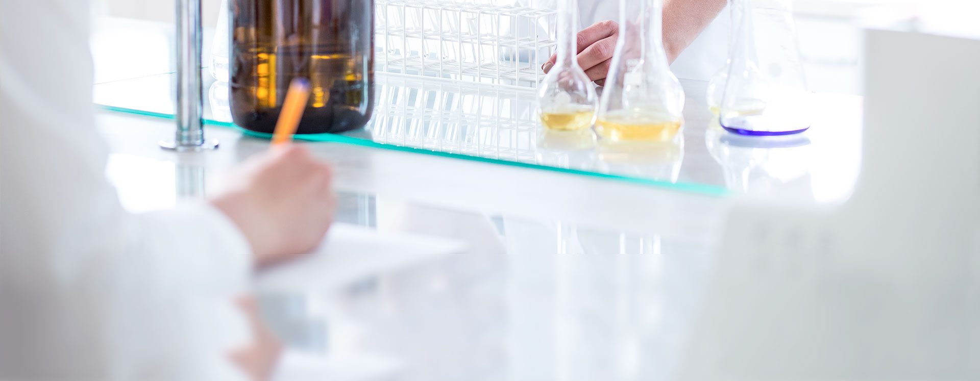 A person dressed in a white apron writing a pen on paper in a laboratory